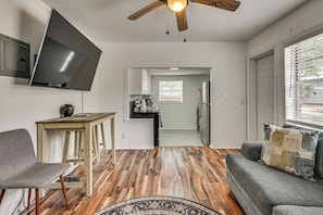 Uma sala de estar moderna com TV de tela plana, ventilador de teto de madeira, sofá e mesa de jantar.