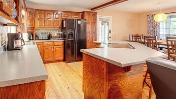 A kitchen with wooden cabinets, a refrigerator, a coffee maker, and a dining area with a table and chairs.