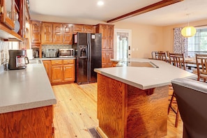 A kitchen with wooden cabinets, a refrigerator, a coffee maker, and a dining area with a table and chairs.