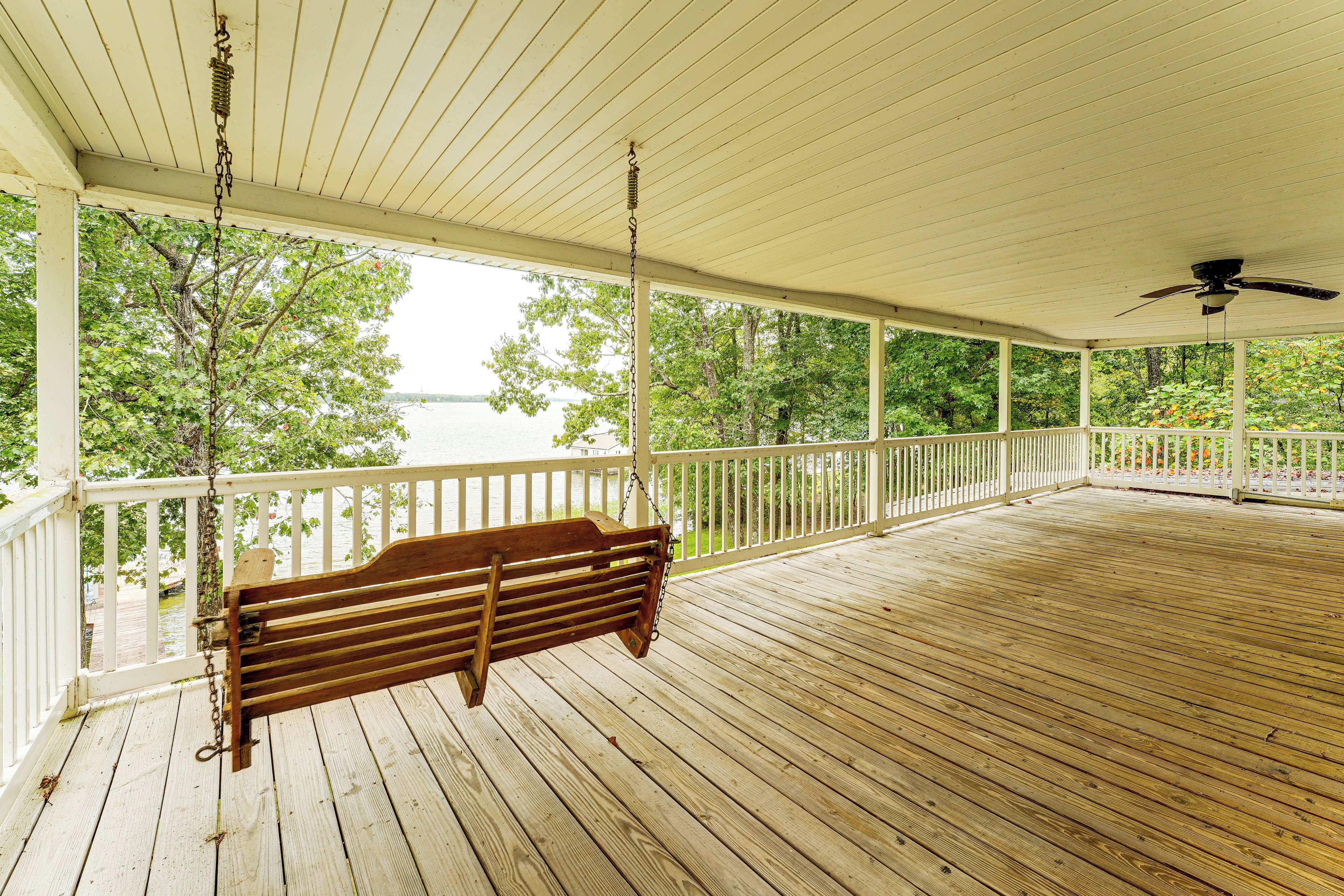 A wooden deck with a swing, white railing, and a view of a body of water.