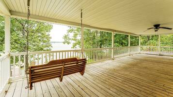 A wooden deck with a swing, white railing, and a view of a body of water.