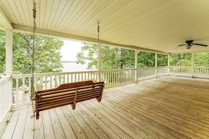 A wooden deck with a swing, white railing, and a view of a body of water.