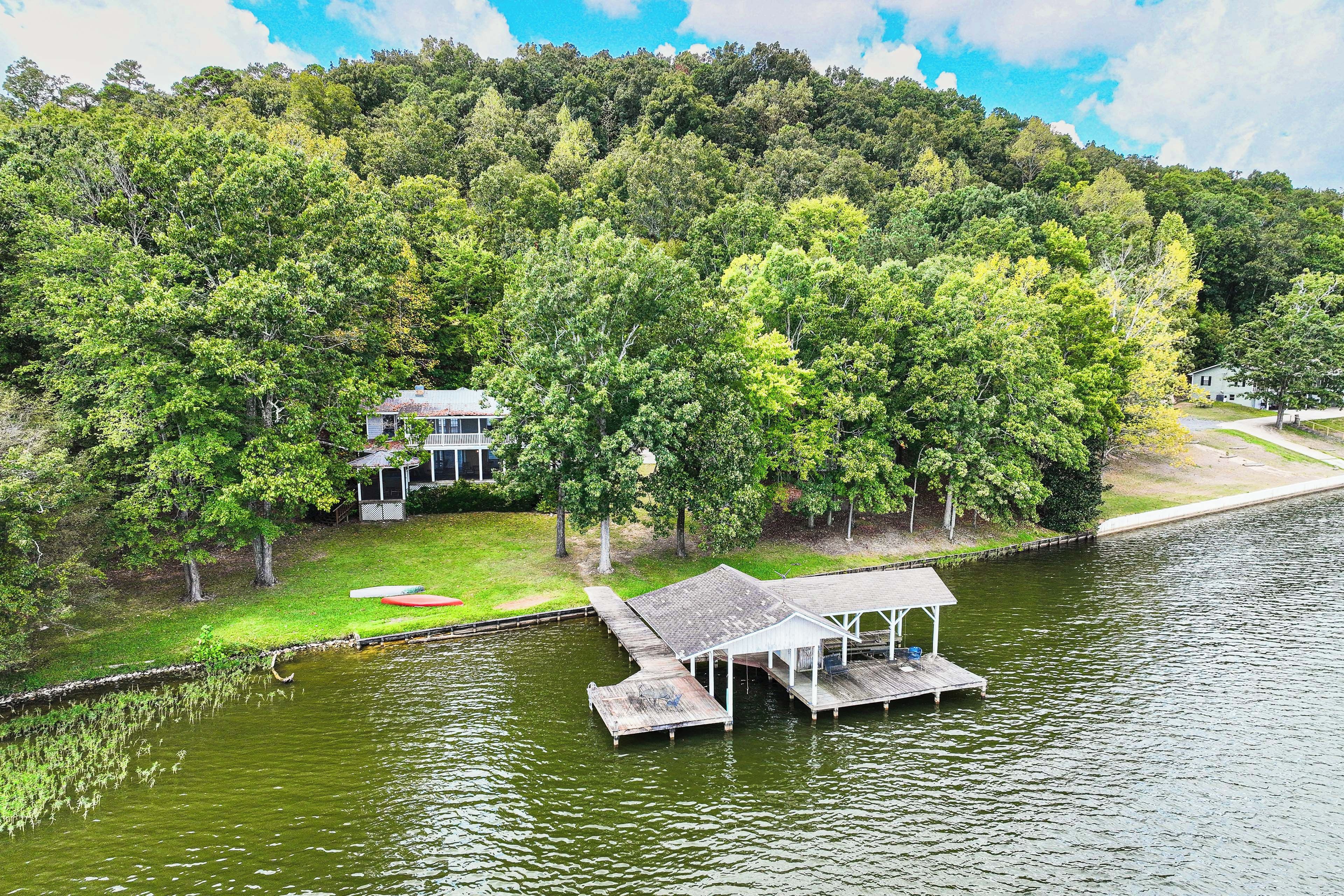 A lakeside property with a dock, a covered boat launch, and a house surrounded by dense forest.