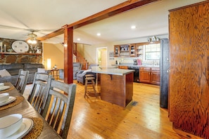 A spacious living area with a wooden dining table, chairs, and a kitchen with wooden cabinets and a stone wall. - Weiss Lake Group Retreat w/ Hot Tub & Fire Pit (Cedar Bluff)