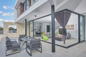 Een terras buiten met een eettafel en stoelen, een bank en een televisie.