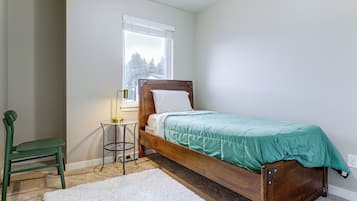 A bedroom with a wooden bed, a green chair, a small round table, and a window with blinds.