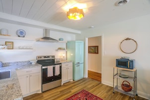 Cocina compacta con estufa, horno y refrigerador, un microondas en un estante, y una alfombra roja en el suelo.