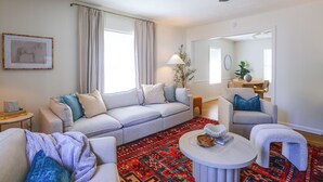 Uma sala de estar com sofá, poltronas, mesa de centro e um tapete estampado.