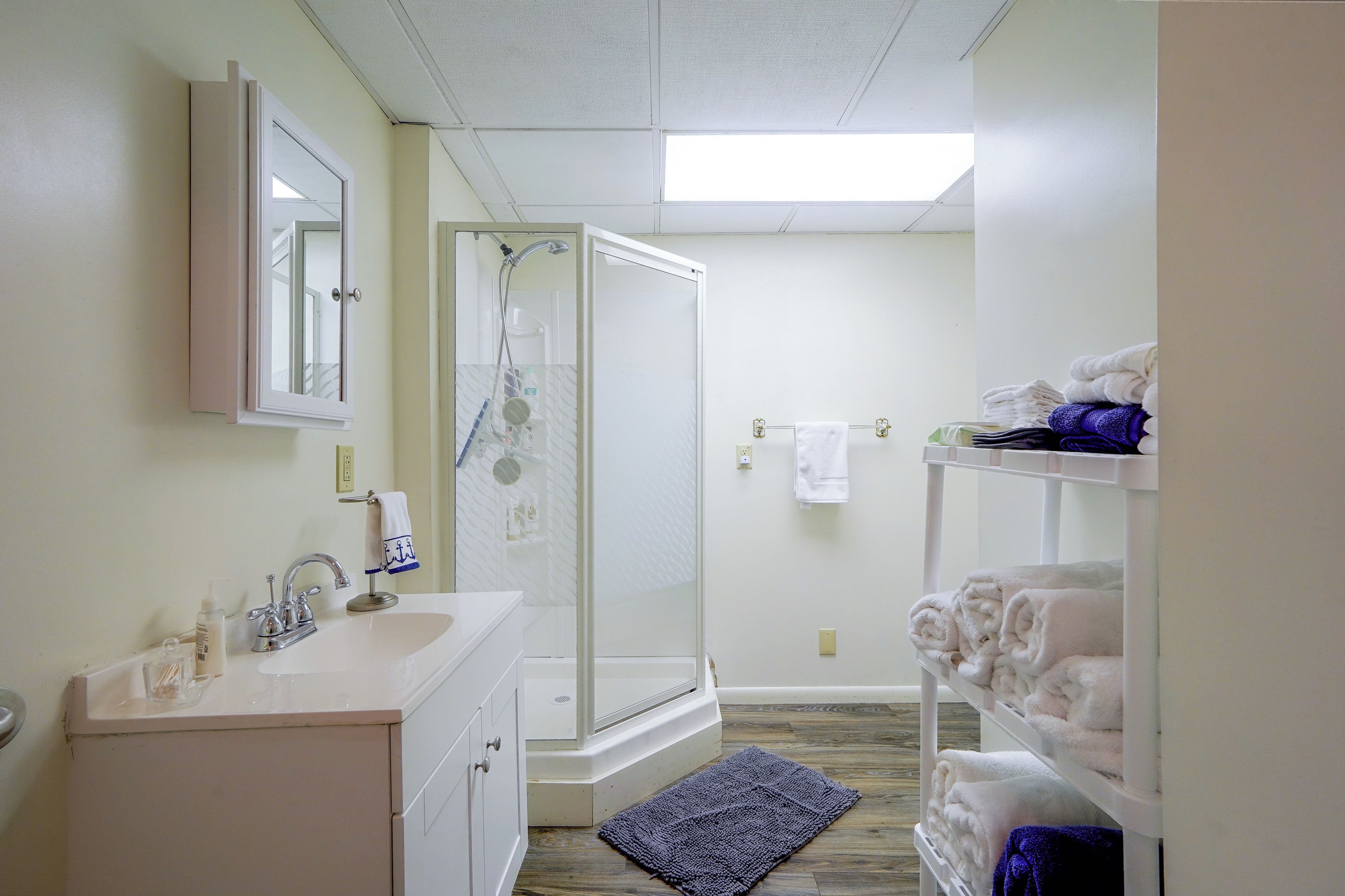 A bathroom with a sink, mirror, shower, and towel rack.