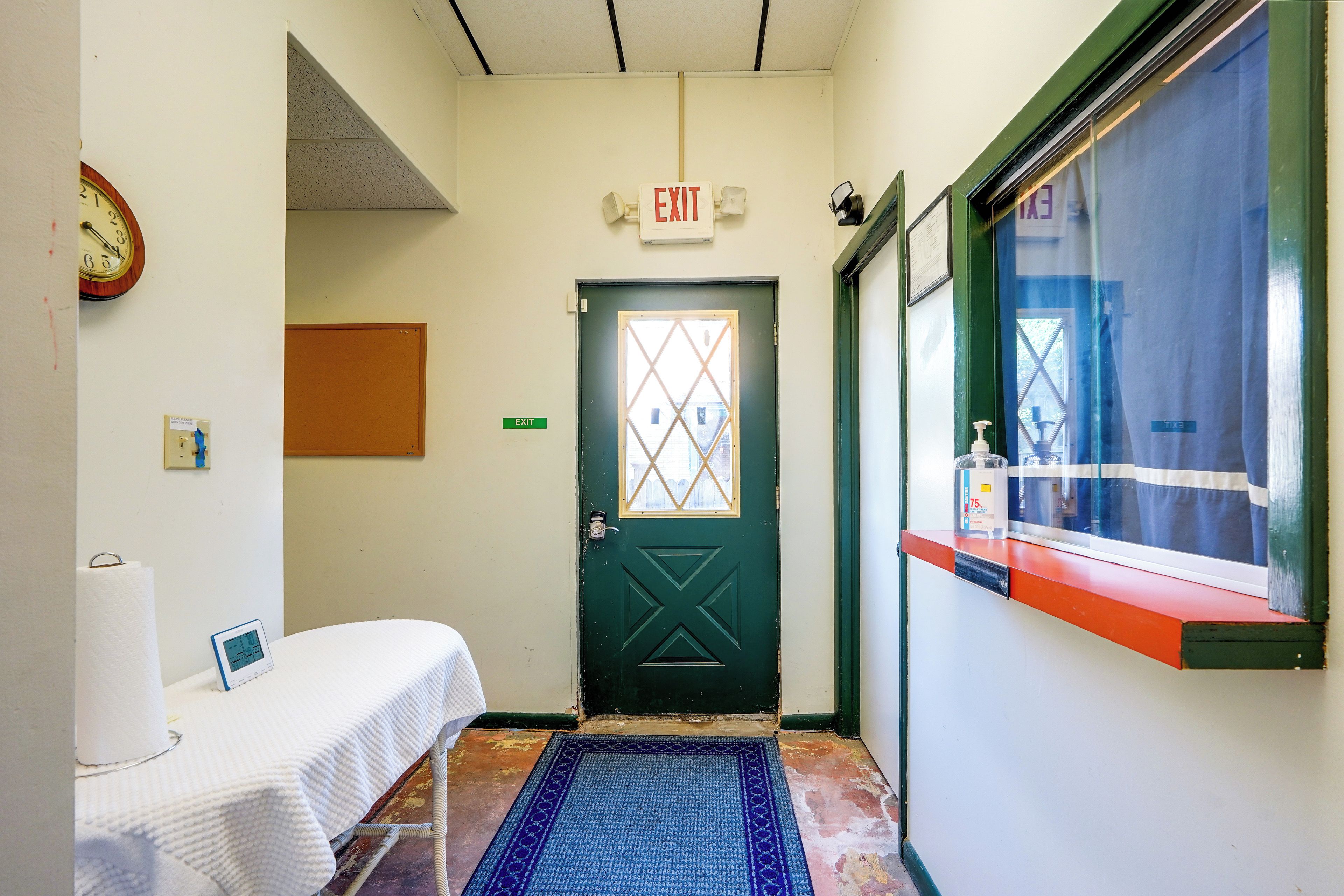 A hallway with an exit door, a clock, a tissue dispenser, and a window with a view.