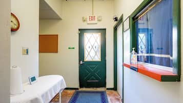 A hallway with an exit door, a clock, a tissue dispenser, and a window with a view.