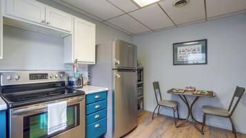 A compact kitchen with a stove, oven, microwave, and refrigerator. There is a small dining table with chairs and a framed picture on the wall.