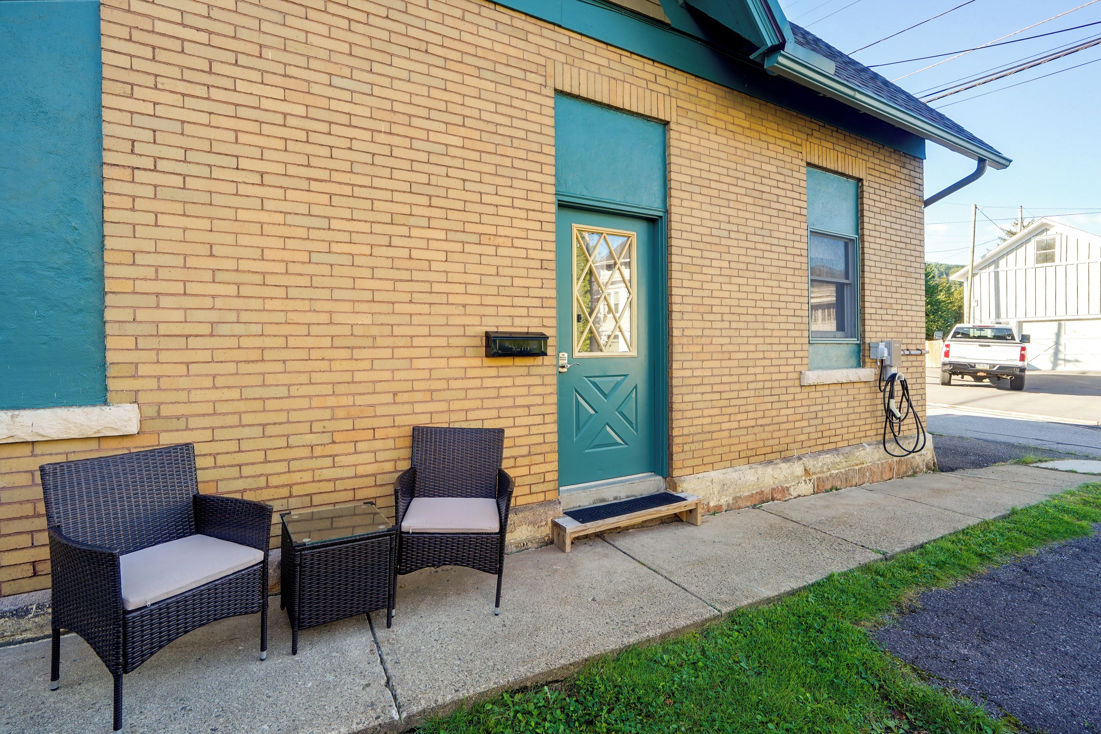 A building with a brick facade, a green door, and a small porch with wicker furniture.
