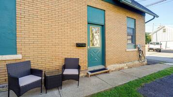 A building with a brick facade, a green door, and a small porch with wicker furniture.