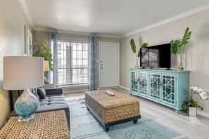 Uma sala de estar com sofá, televisão em um móvel e janela com cortinas.