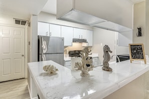 Una cocina moderna con armarios blancos, electrodomésticos de acero inoxidable y esculturas decorativas de coral en la encimera.