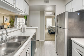 Cozinha moderna com eletrodomésticos de aço inoxidável, pia dupla e vista para o quarto adjacente.