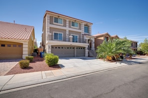 A residential area with a two-story house featuring a garage, a driveway, and a well-maintained lawn with small shrubs. - Multi-level Group Haven! 9 Mi to Allegiant Stadium (Las Vegas)