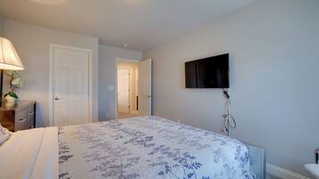 Un dormitorio con una cama, un televisor montado en la pared y una puerta que da a otra habitación.