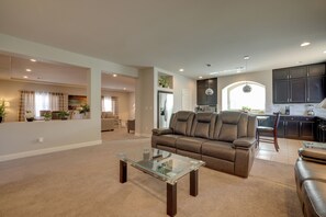 A spacious living room with a leather sofa, a glass coffee table, and a kitchen area in the background.