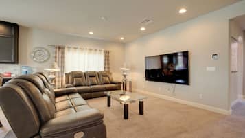 A living room with a sectional sofa, a flat-screen TV, and a glass coffee table.