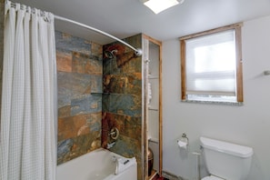A bathroom with a shower, a toilet, and a window.