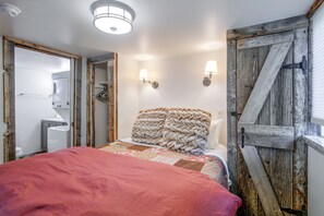 A bedroom with a bed, a wooden door, a wall-mounted light fixture, and a ceiling light. - Mtn Views & Trail Access! Driggs Couple's Getaway (Victor)