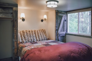 A bedroom with a bed, two wall-mounted lamps, a window with a view of trees, and a wooden headboard.