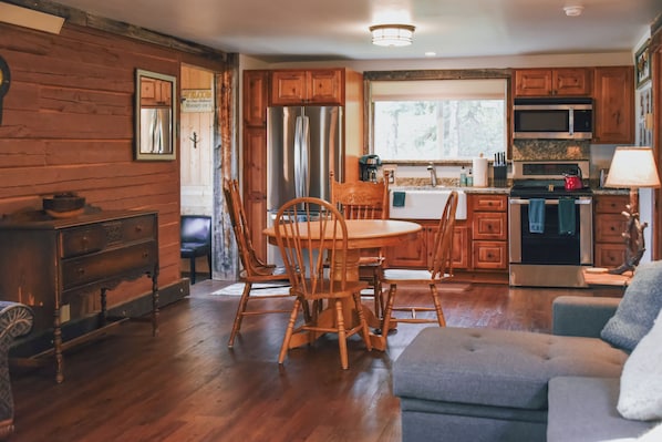 A cozy kitchen with wooden cabinets, a dining table with chairs, a refrigerator, and a microwave.