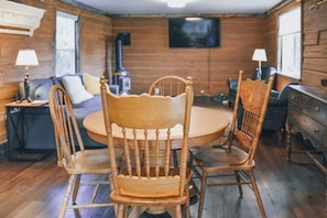 A wooden dining table with chairs, a television mounted on the wall, and a sofa in a room with wooden walls and floors.