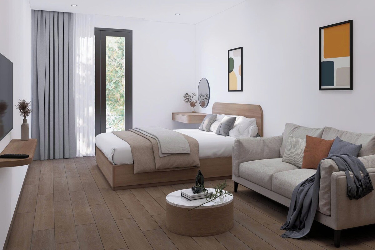 A modern bedroom with a bed, a sofa, a bedside table, a mirror, and artwork on the walls.