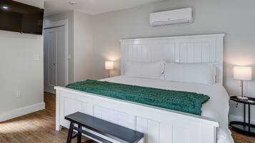 A bedroom with a bed, bedside lamps, a bench, an air conditioning unit, and a door.