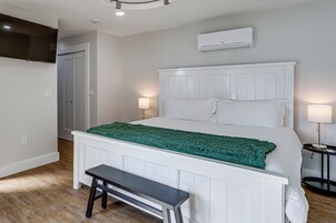 Un dormitorio con cama, lámparas de noche, una banca, un equipo de aire acondicionado y una puerta.