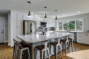 Uma cozinha moderna com armários brancos, eletrodomésticos de aço inoxidável e uma ilha grande com banquetas.