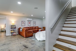 Sala de estar com um sofá em couro marrom, tapete branco e escada que leva a um andar superior.