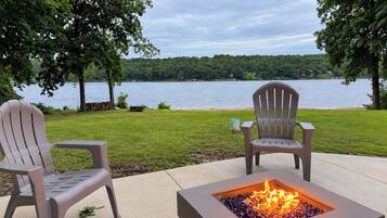 Un foyer extérieur avec vue sur un lac, deux fauteuils Adirondack et une zone herbeuse.
