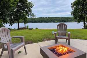 Una fogata con vista a un lago, dos sillas Adirondack y una zona de césped.