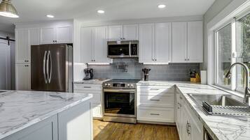 A modern kitchen with white cabinetry, stainless steel appliances, and a marble countertop.