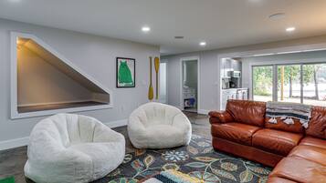 Un salon moderne avec un canapé en cuir marron, deux fauteuils en forme de poire blancs, un tapis coloré et un tableau représentant un chat accroché au mur.