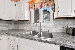 A kitchen with white cabinets, a double sink, and a window with a floral curtain.