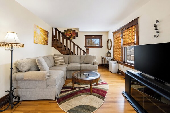 A living room with a sectional sofa, a coffee table, a TV, a staircase, and artwork on the walls.