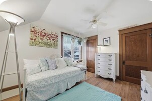 Un dormitorio con cama, cómoda, ventilador de techo y ventana con persianas.