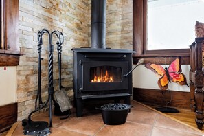 A wood-burning stove with a fire burning inside, placed on a tiled floor.