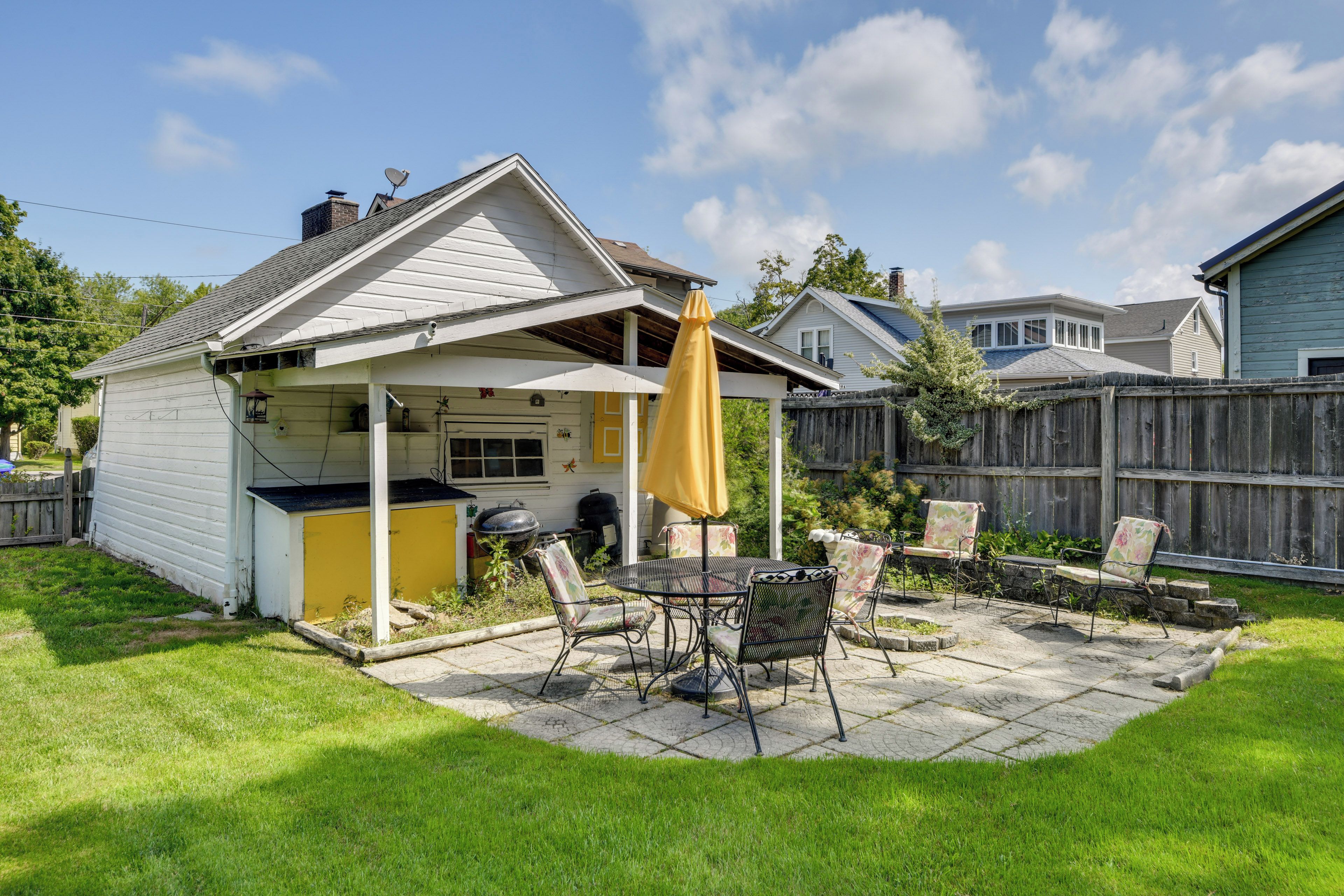 A backyard with a patio, a barbecue grill, and a yellow umbrella.