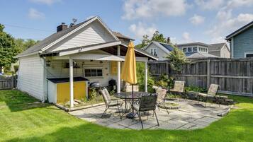 A backyard with a patio, a barbecue grill, and a yellow umbrella.