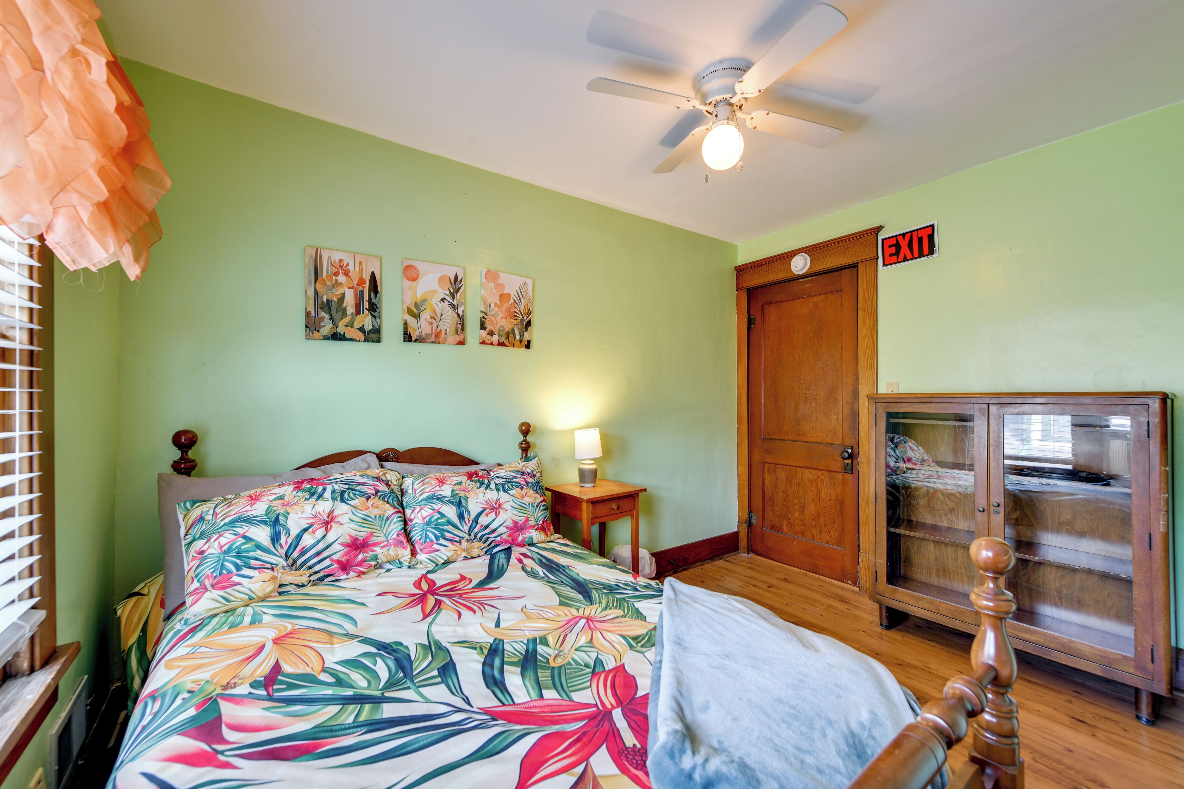 A bedroom with a bed, a ceiling fan, a nightstand, an exit sign, and a wooden cabinet.