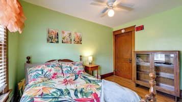 A bedroom with a bed, a ceiling fan, a nightstand, an exit sign, and a wooden cabinet.