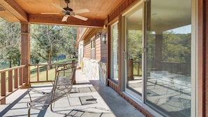 A covered outdoor seating area with a metal chair, a ceiling fan, and a view of a lake and trees. - Mtn Views, On the White River: Norfork Getaway (Norfork)