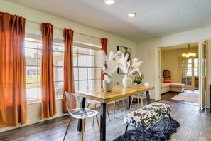 A dining area with a wooden table, clear chairs, and a bench. There are large windows with curtains, a vase with white flowers, and a painting on the wall. - Families w/ Pets Welcome! Retreat 14 Mi to Tampa (Brandon)