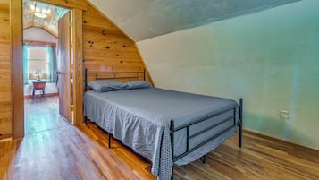 A bedroom with a sloped ceiling, wooden walls, a bed with a patterned bedspread, and a visible door leading to another room.
